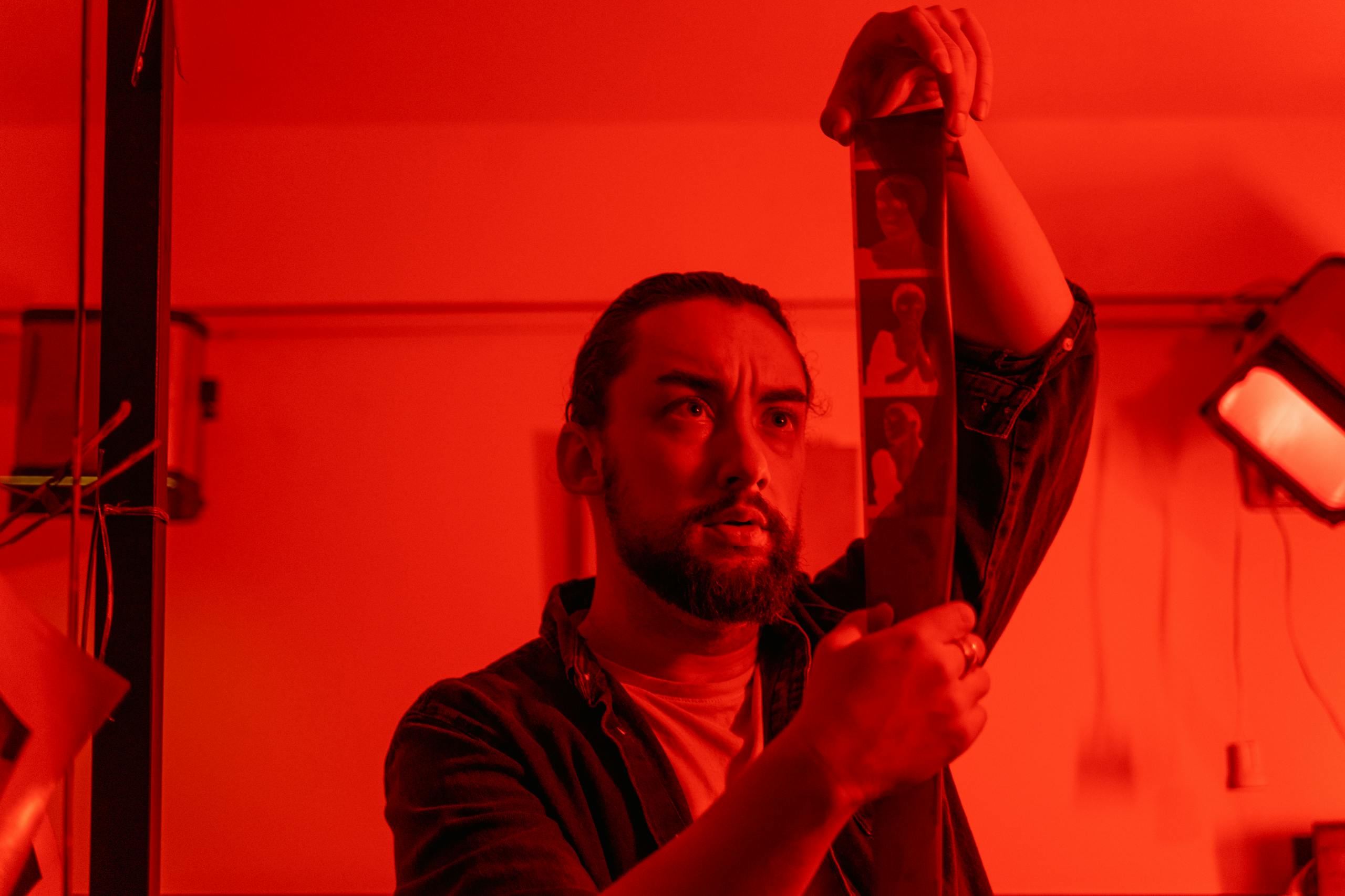 Photographer examining film negatives under red light in a darkroom.