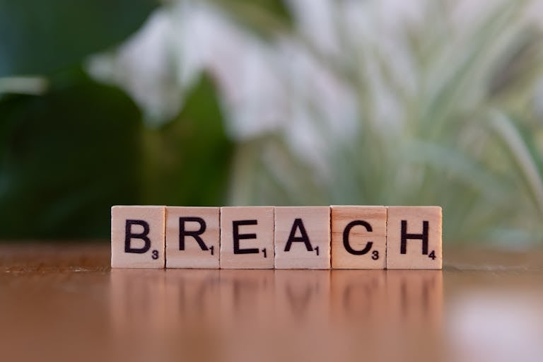 Wooden letter tiles spell 'Breach' against a blurred natural background, concept of security or violation.