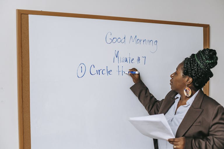 A professional woman in a classroom writing on a whiteboard during a lecture session.