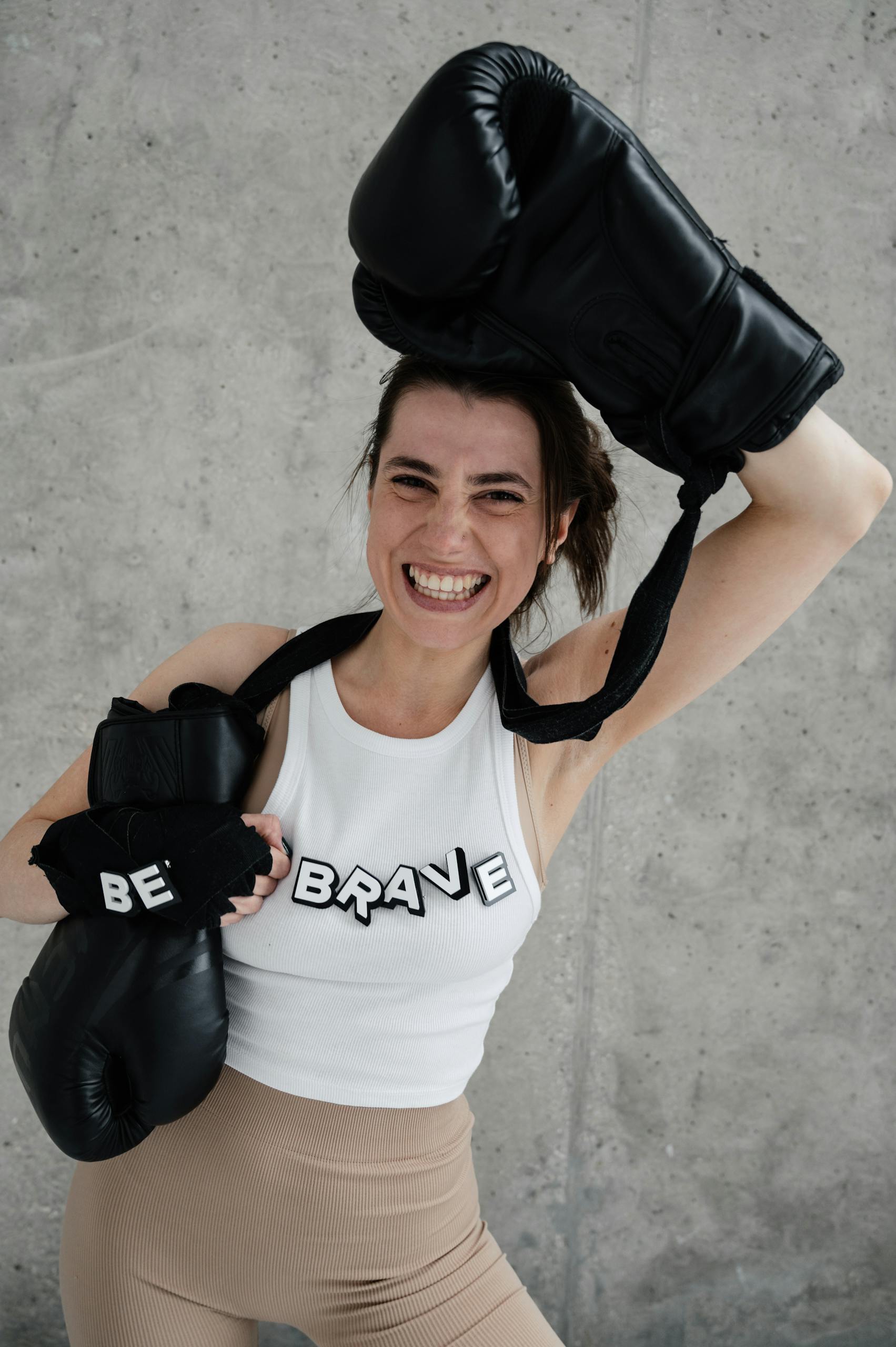 Confident woman smiling with boxing gloves and 'be brave' shirt, showcasing empowerment.